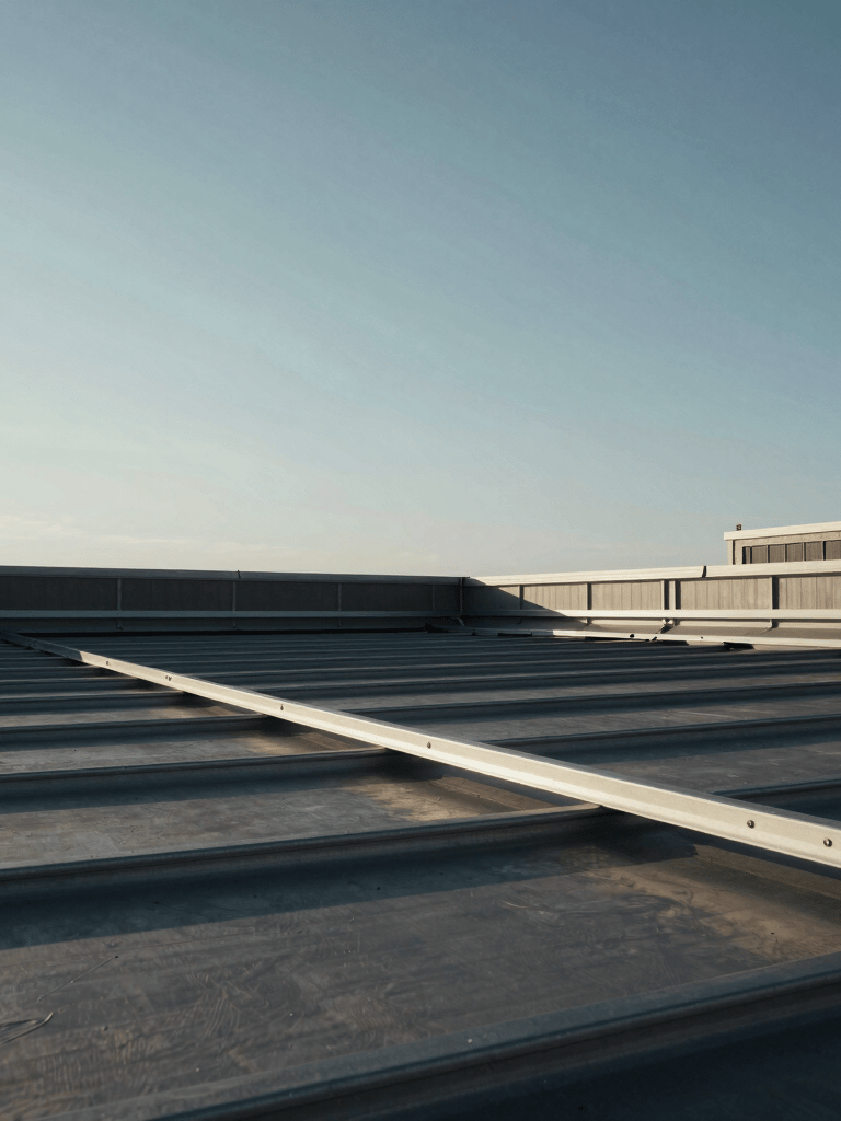 Low angle shot of a large industrial roofing project in North American / NYC, steel gray sky, high-contrast lighting, sharp architectural lines against a clear morning sky.
