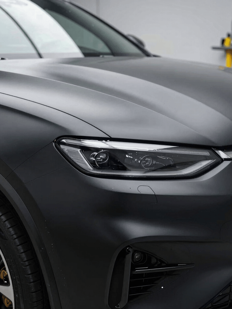 A close-up of a high-end luxury vehicle being wrapped in matte black foil, showing the precision of the edges and the smooth texture, professional workshop lighting, Northern European setting.