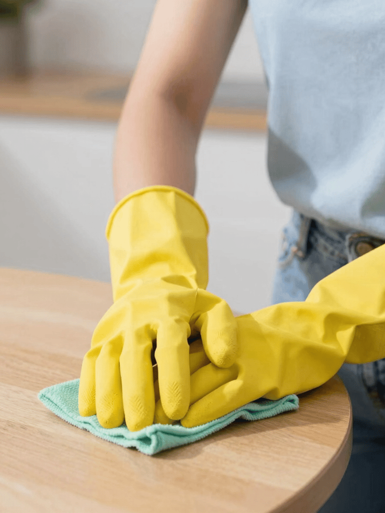 a woman in a striped shirt and yellow gloves is cleaning a table