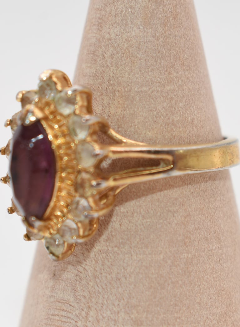 Vintage gold tone ring featuring a large oval red ruby color w/rhinestone halo setting.