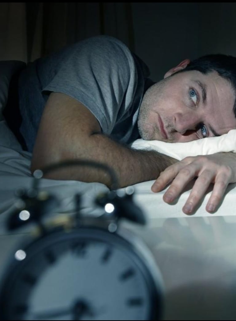 a man lying in bed with a clock on the side
