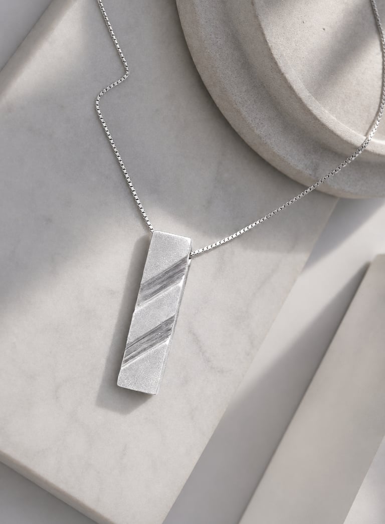 Handcrafted modern 999 fine silver pendant necklace displayed on a white marble surface.