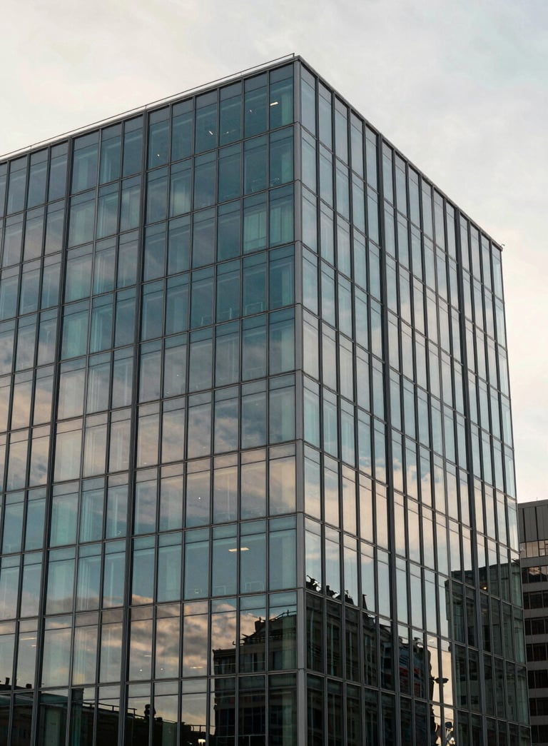 A wide shot of a modern architectural glass building reflecting a soft off-white morning sky. The image has a professional and corporate feel with muted teal and steel blue accents in the glass panes.