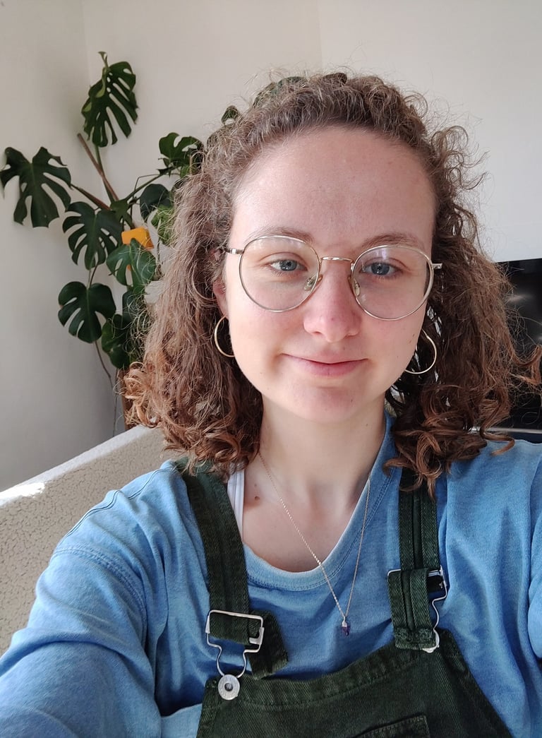 a selfie of Eleanor who is a curly haired queer women in her late twenties wtih glasses and dungarees