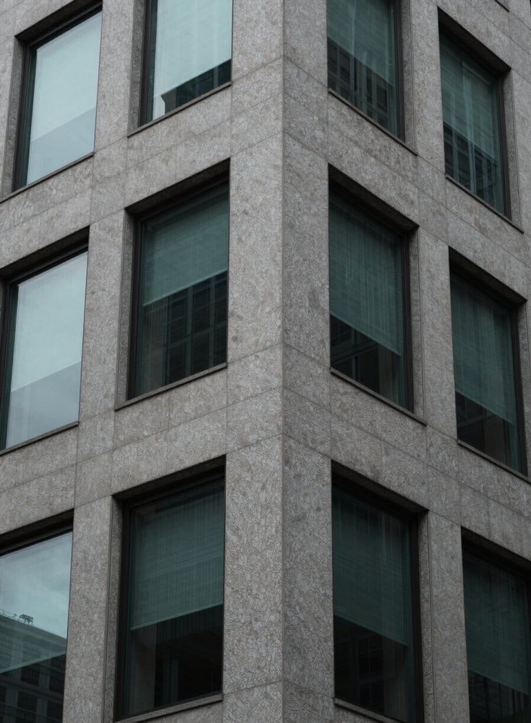A close-up, minimalist architectural photograph of a sleek office building corner in North America, focusing on textures of gray stone and dark glass with soft teal reflections.