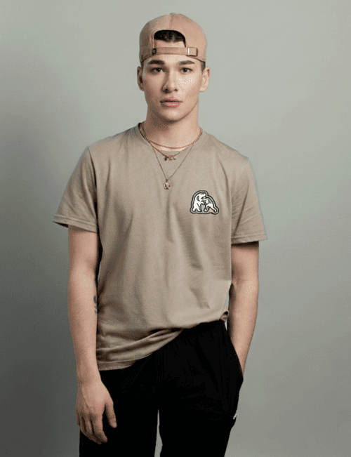 Joven usando una camiseta color beige de cuello redondo y una gorra, posando frente a un fondo gris.