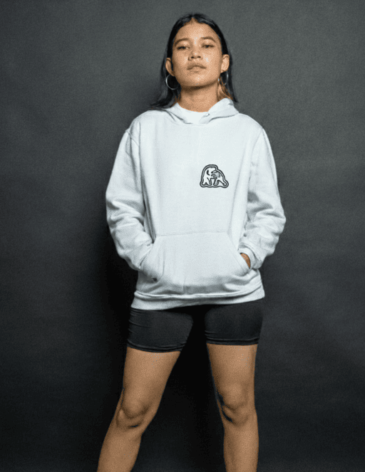 Una joven vistiendo una sudadera blanca con estampado gráfico y shorts, posando en fondo gris.