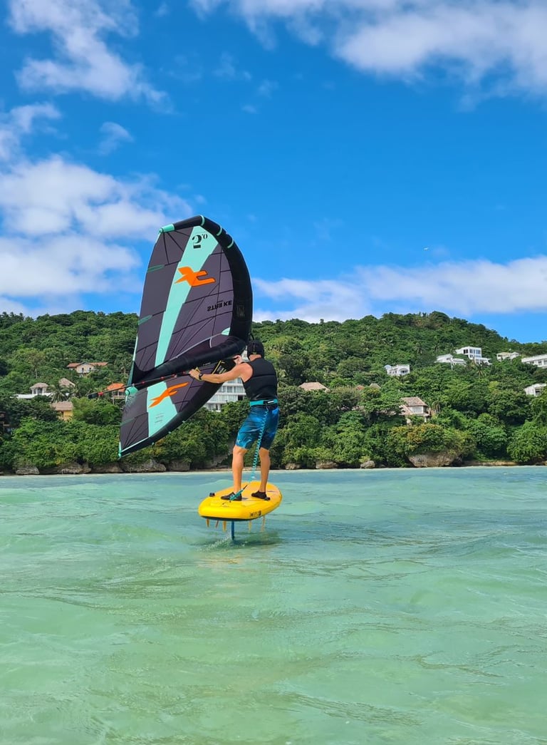 a man holding a wing on a beginner foil board in the middle of crystal clear water in a lagoon