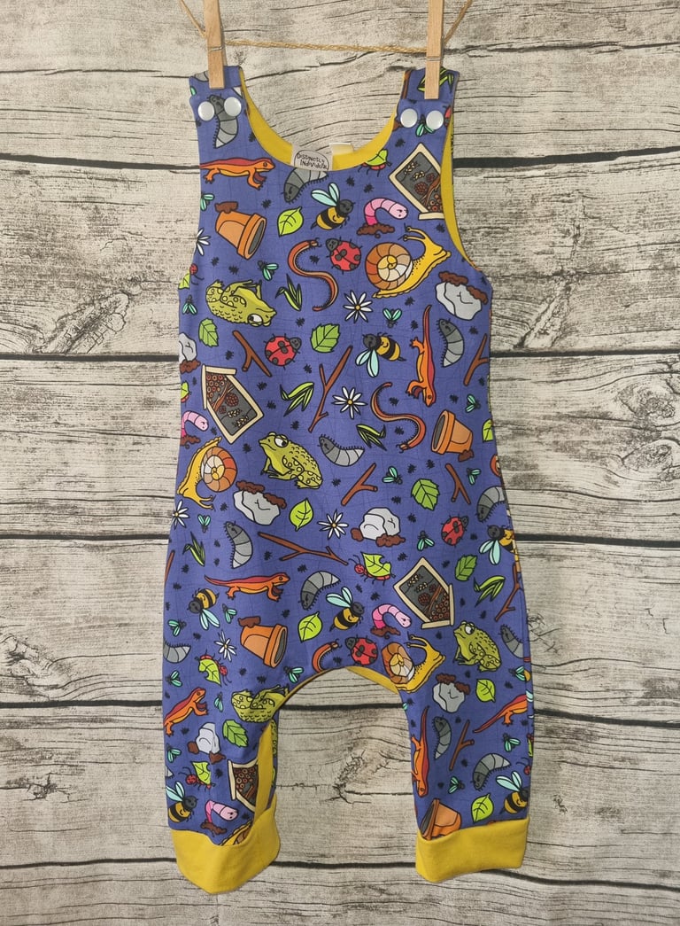 a baby's overalls with a blue and yellow romper with garden creatures forest school print
