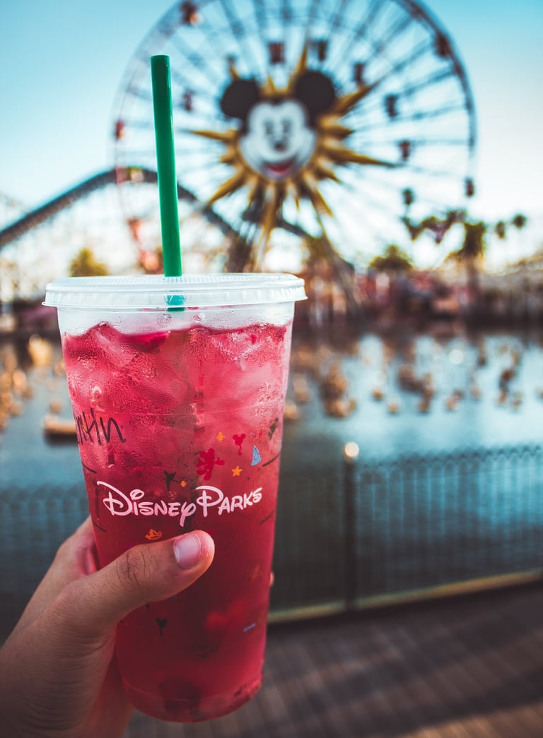 a person holding a cup of drink in front of a ferris wheel