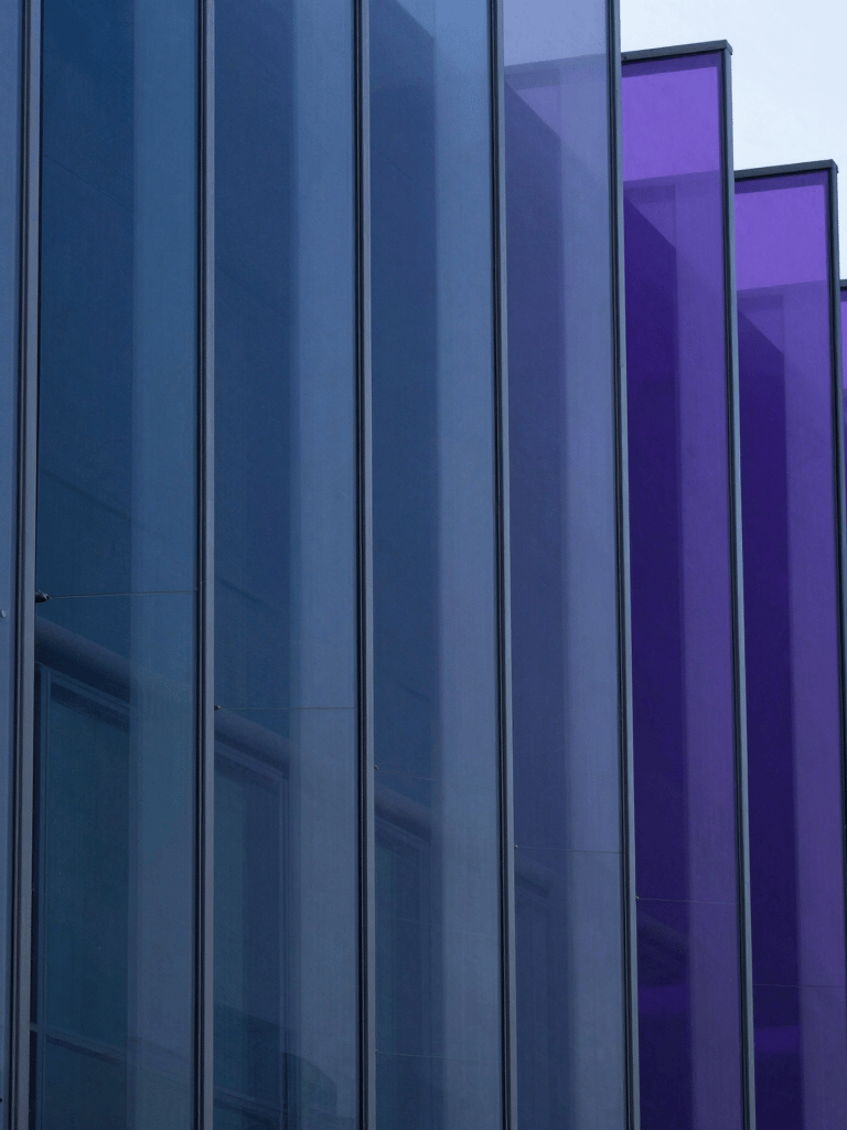 A sophisticated abstract close-up of layered glass panels catching light in gradients of indigo blue and deep violet. The composition is clean and minimalist, conveying a sense of structure and innovation in a North American architectural context.