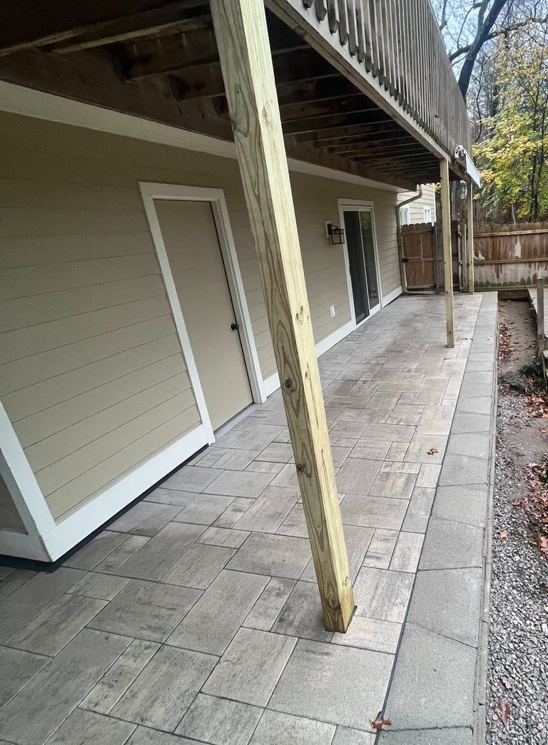 Backyard patio with grey stone pavers installed underneath a raised wooden deck.