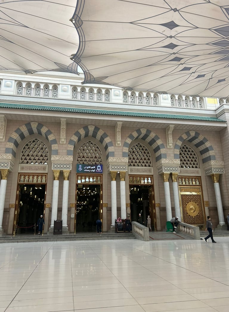 Grand entrance of Al-Masjid an-Nabawi in Medina with ornate arches and large umbrellas.