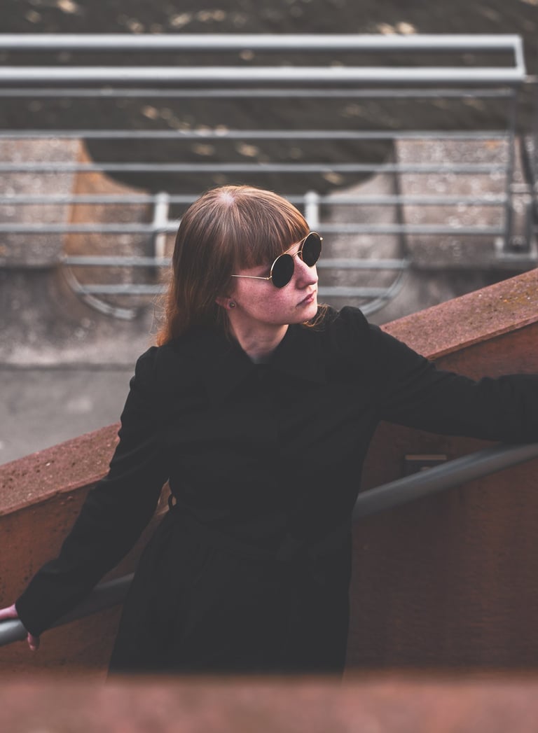 a woman in sunglasses and a black jacket standing on a stair case
