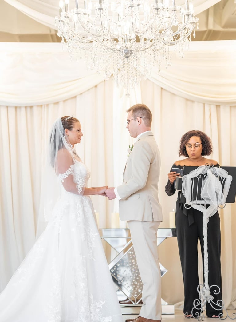 Bride and groom exchanging wedding vows under a crystal chandelier with an officiant.