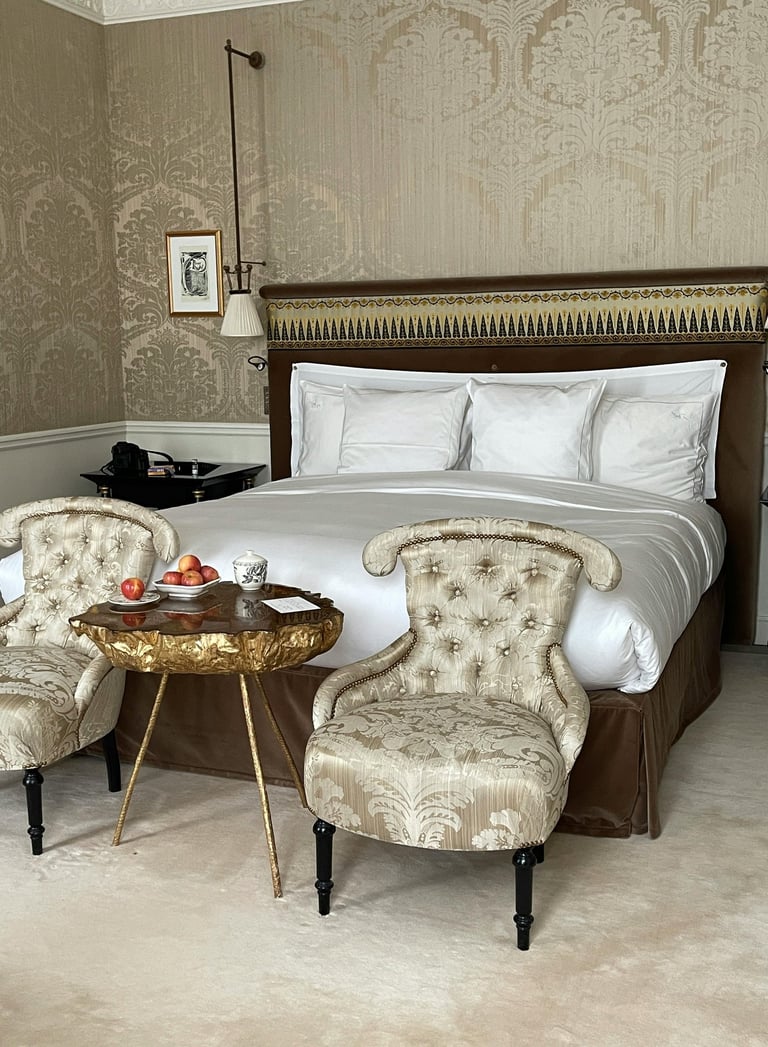 Habitación de hotel de lujo con cama en el medio y 2 sillones y una mesa delante.