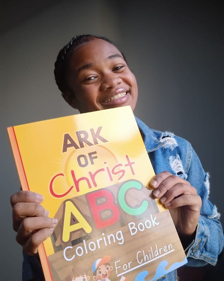 Smiling young girl holding up an Ark of Christ ABC Coloring Book for Children.