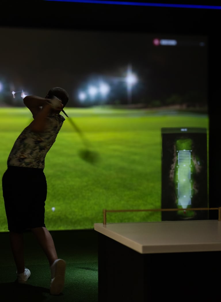 A golfer hitting a shot in a premium indoor golf simulator bay at 1IRON indoor golf