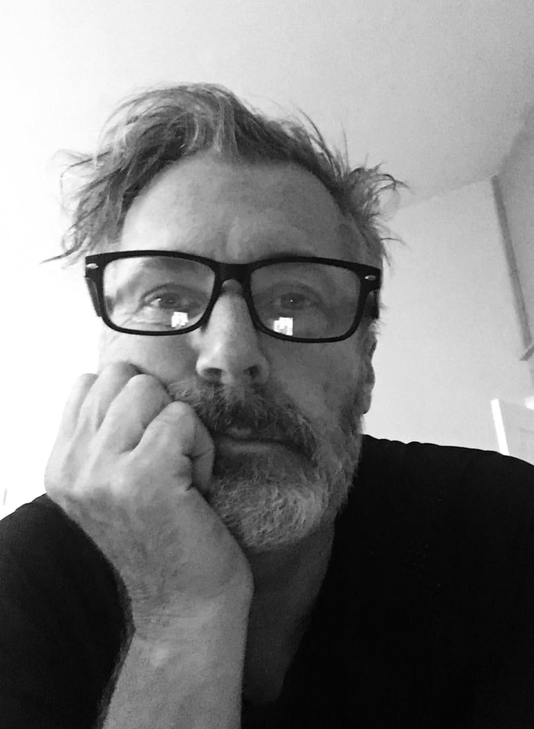 Black and white portrait of a man with glasses and a beard resting his chin on his hand.