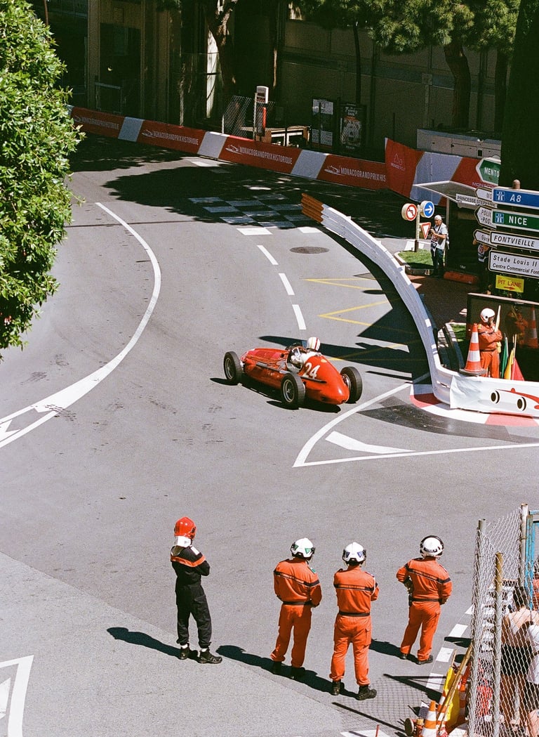 a group of race marshals watching a red race car go through a corner