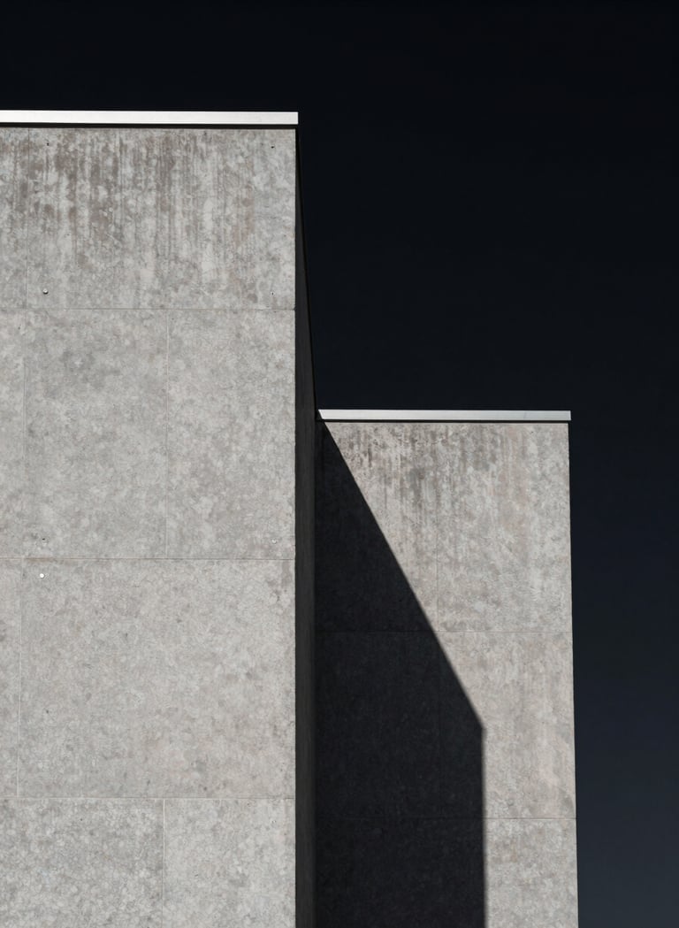 A minimalist architectural detail of a North American building, featuring sharp concrete angles against a deep black sky. The composition is clean and focuses on the texture of the medium gray stone and the dramatic shadow cast by the afternoon sun.