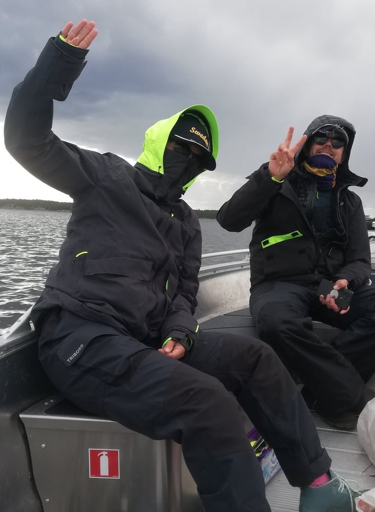 two people in black jackets and green pants sitting on a boat