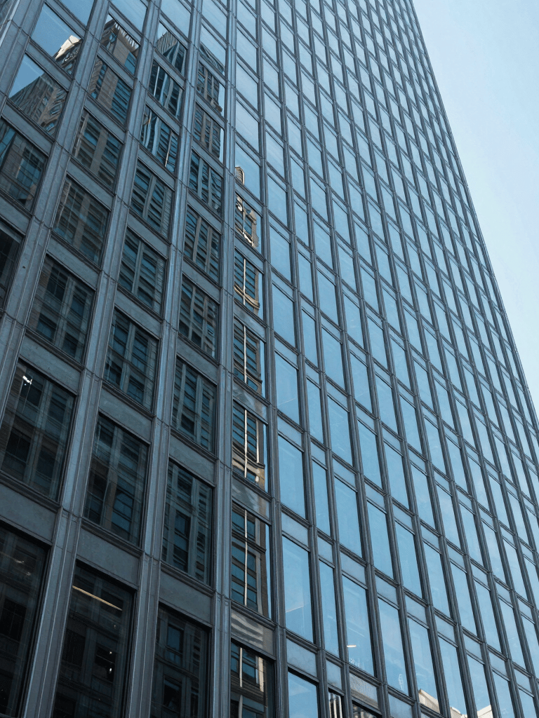 Abstract low-angle shot of a modern glass and steel skyscraper in New York, reflecting a clear light blue sky, emphasizing sharp geometric lines and cutting-edge architectural design.