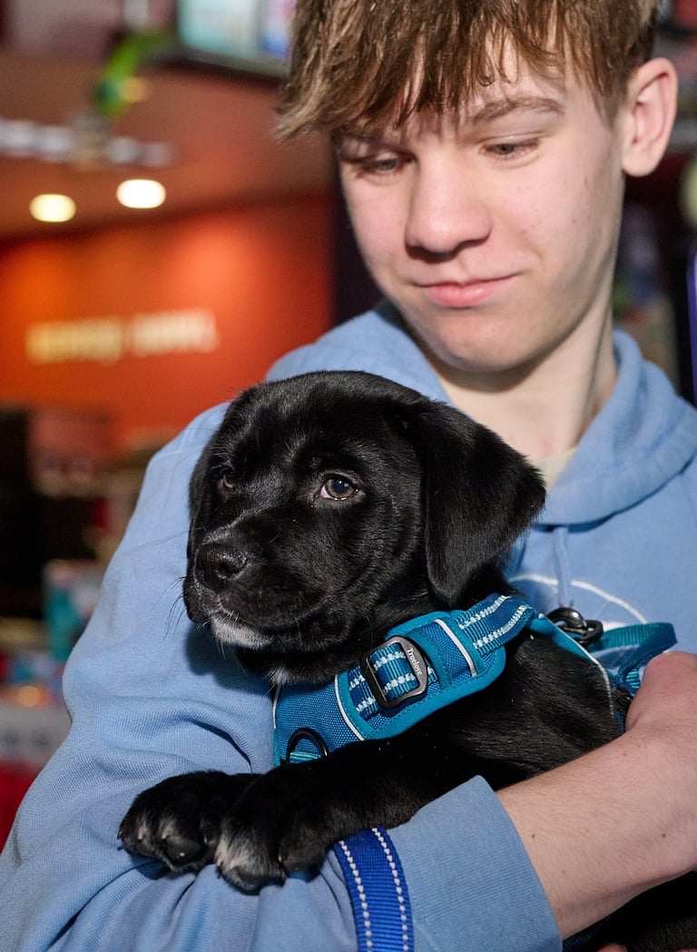 a teenage boy in a blue jacket holding a black puppy
