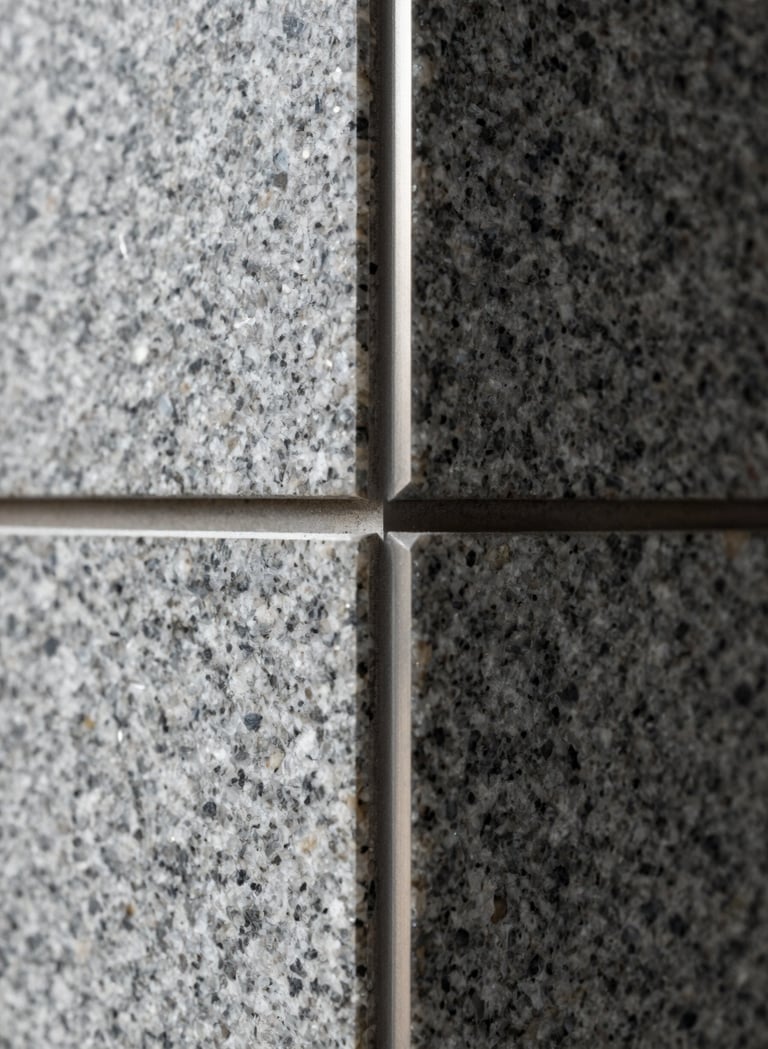 Macro detail shot of tectonic structural joints in the building. A combination of smooth granite gray surfaces and precise metal finishings, highlighting the studio's technical rigor and high-quality craftsmanship.