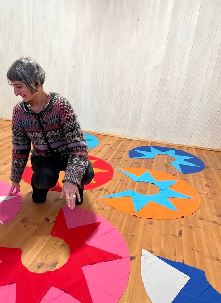 samuko arranging colorful star-patterned fabric circles on a wooden floor for a textile project.
