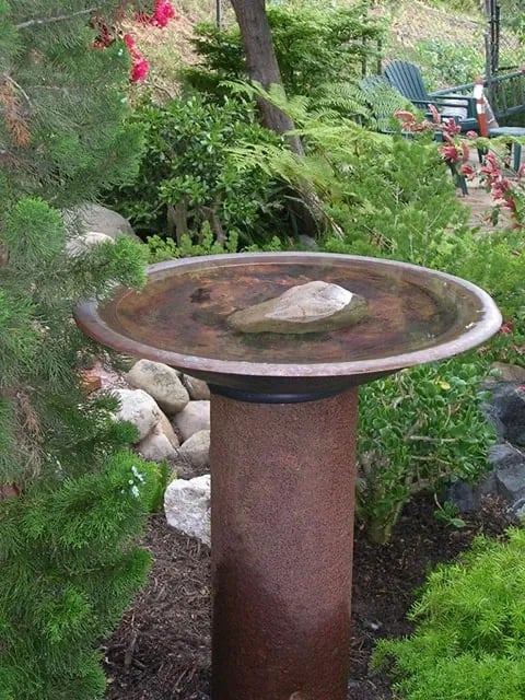 A birdbath made of a copper firepit and old rusted pipe.
