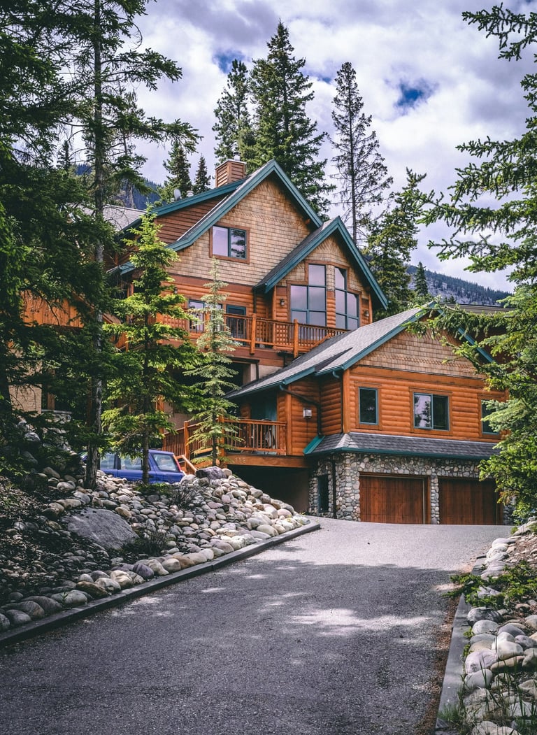 Luxury rustic log cabin with stone driveway nestled in a dense evergreen mountain forest.