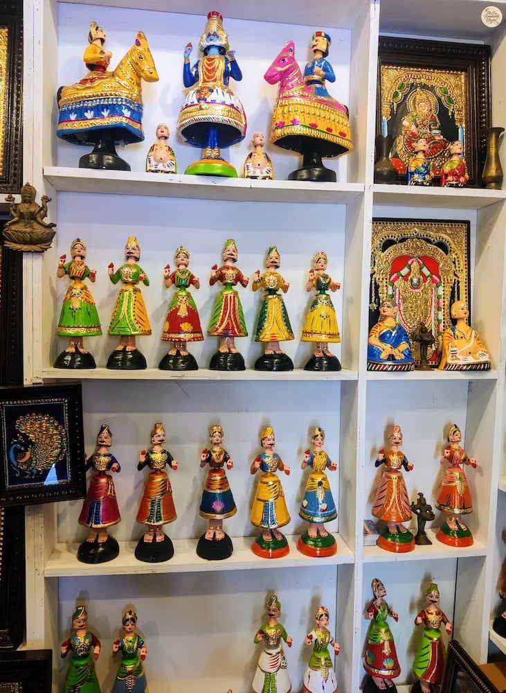 Colorful Thanjavur dolls alongside framed Thanjavur paintings for sale in Tamil Nadu