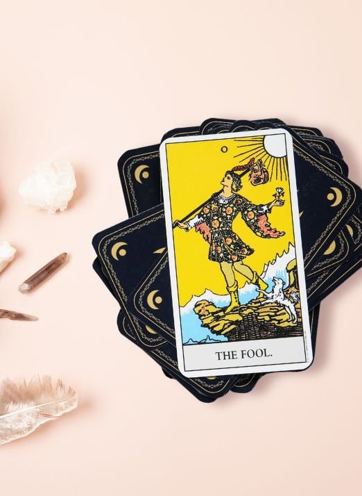 The Fool tarot card on a stack with crystals used in beginner tarot course.
