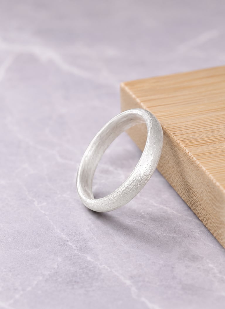 Handmade brushed 999silver wedding band resting against a wooden block on a marble surface.