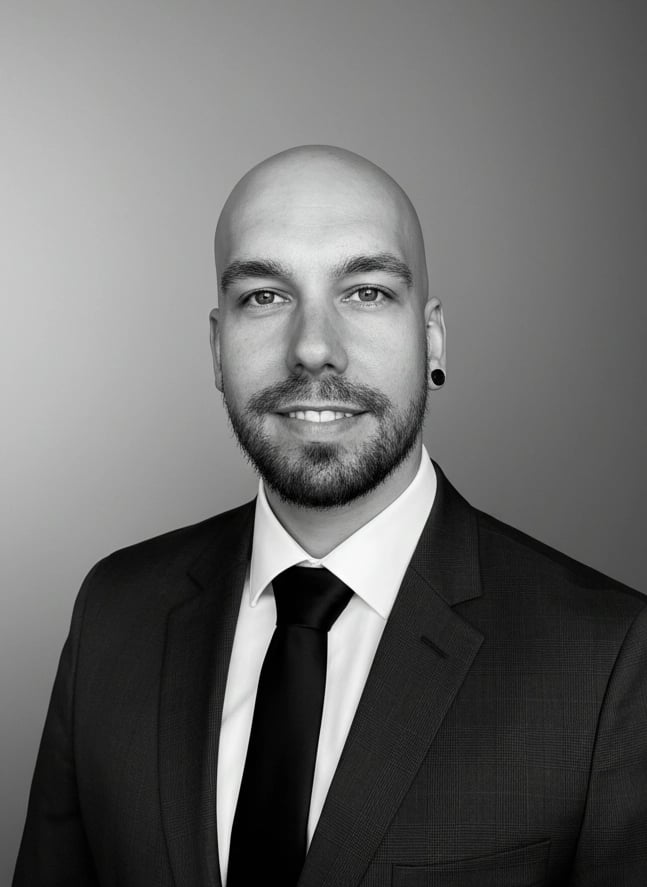 Professional black and white headshot of a bald man with a beard wearing a formal suit and tie.