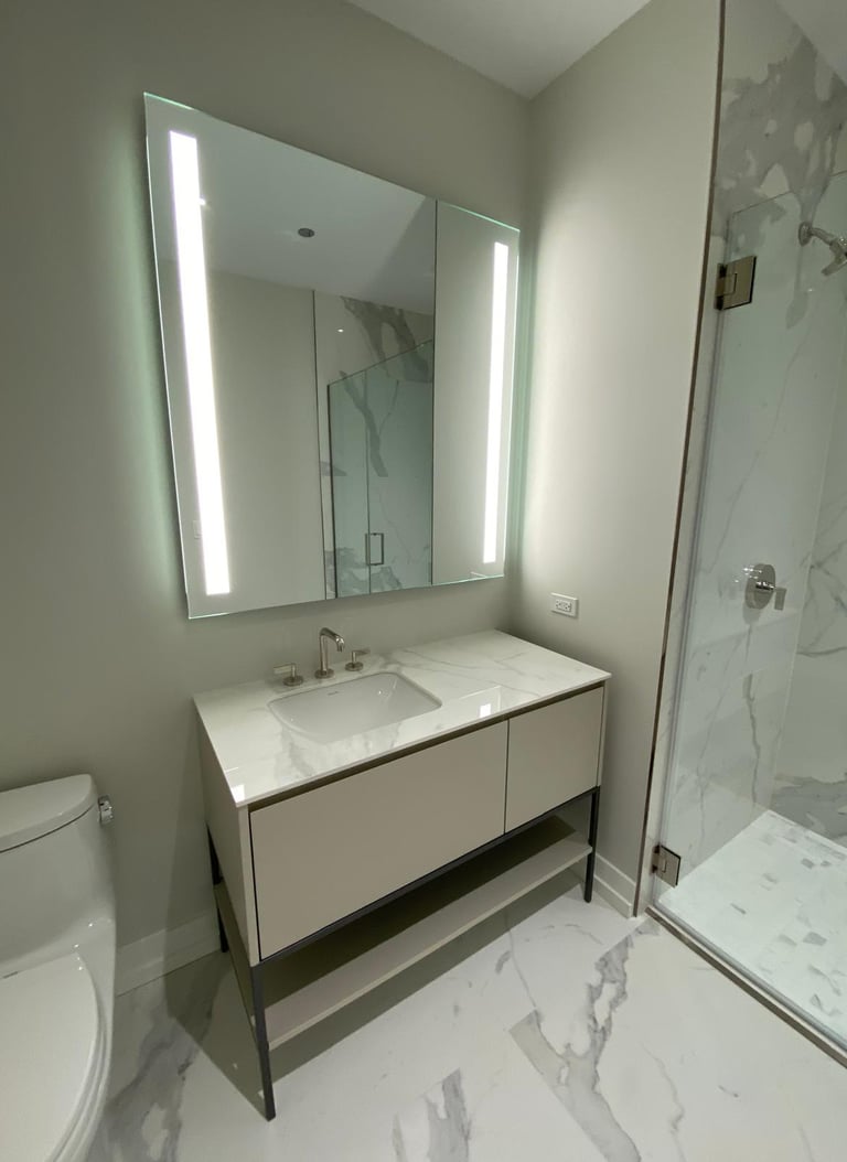 Modern bathroom featuring a light beige vanity, backlit LED mirror, and a marble tile walk-in shower.