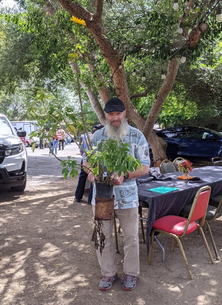 Man holding a tall plant in two stacked pots, with a slight smile