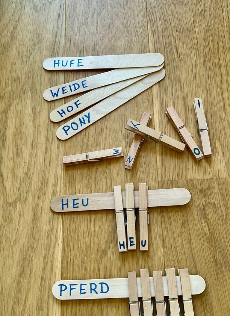 Educational word matching activity using wooden craft sticks and clothespins on a wood floor.
