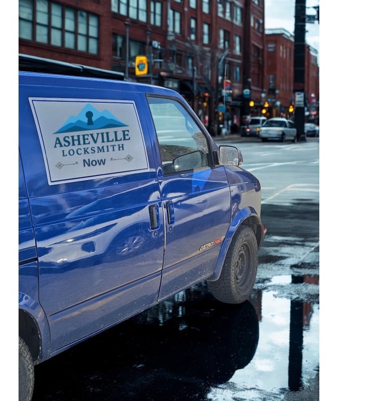 Blue Asheville Locksmith Now service van driving through West Asheville on rainy day