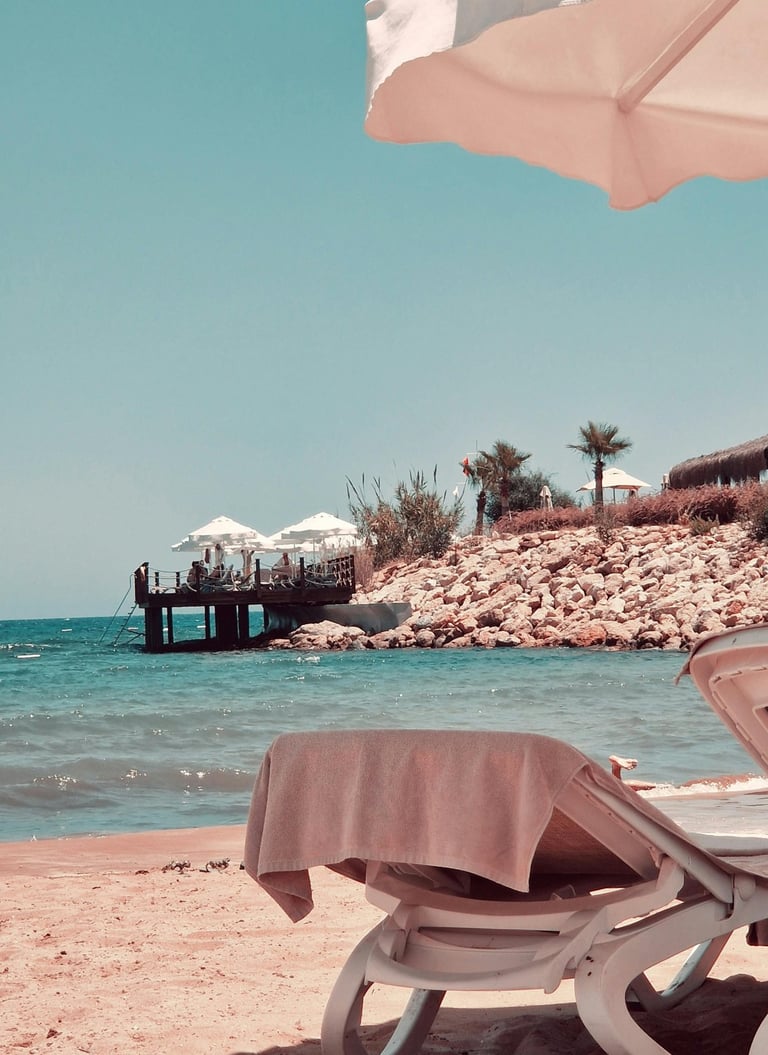 Luxury beach resort with sun loungers, turquoise ocean water, and a wooden pier under a blue sky.