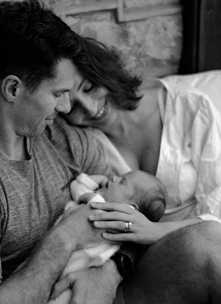 a newborn in her mom & dads arms, looking down at her in a lifestyle newborn shoot