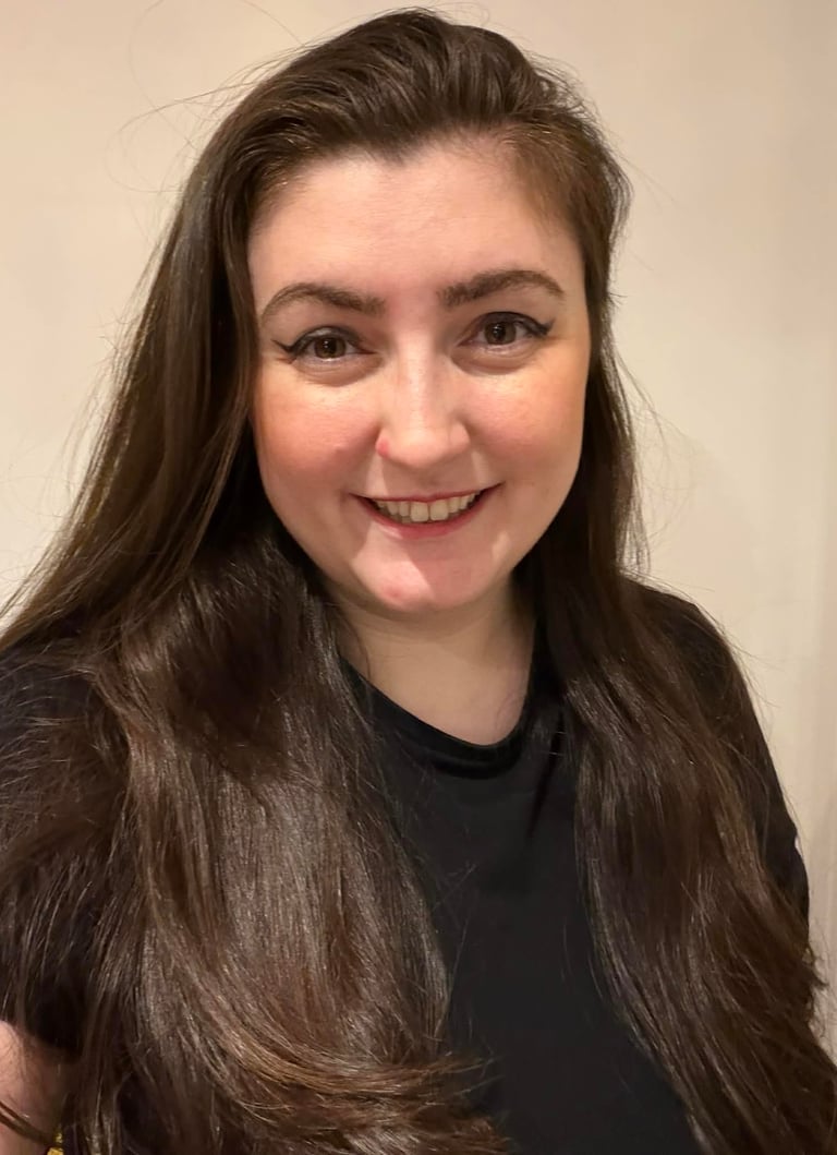 Smiling woman with long dark brown hair and winged eyeliner wearing a black shirt.