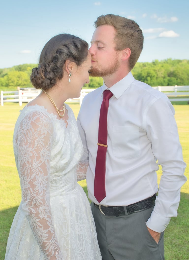 a groom kissing his bride's forehead in a farmland