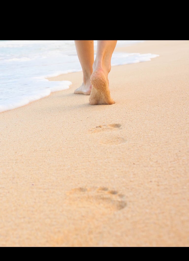 Close-up van voeten op een strand met voetafdrukken in het zand bij de kustlijn.
