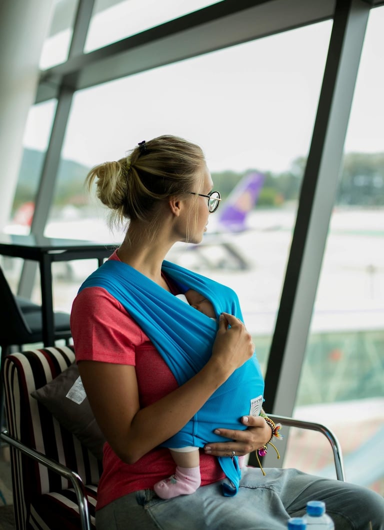 A woman sits in an airport lounge holding a baby in her arms while waiting near the boarding area