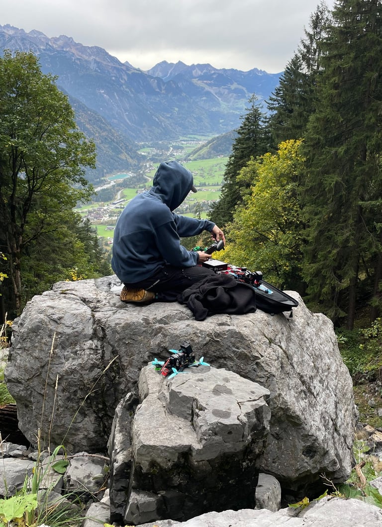 a man sitting on a rock with a backpack building up his drone setup with crossfire and googles