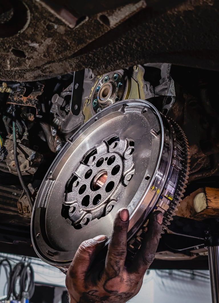 A mechanic holding a high-performance steel flywheel during a car engine and clutch repair.