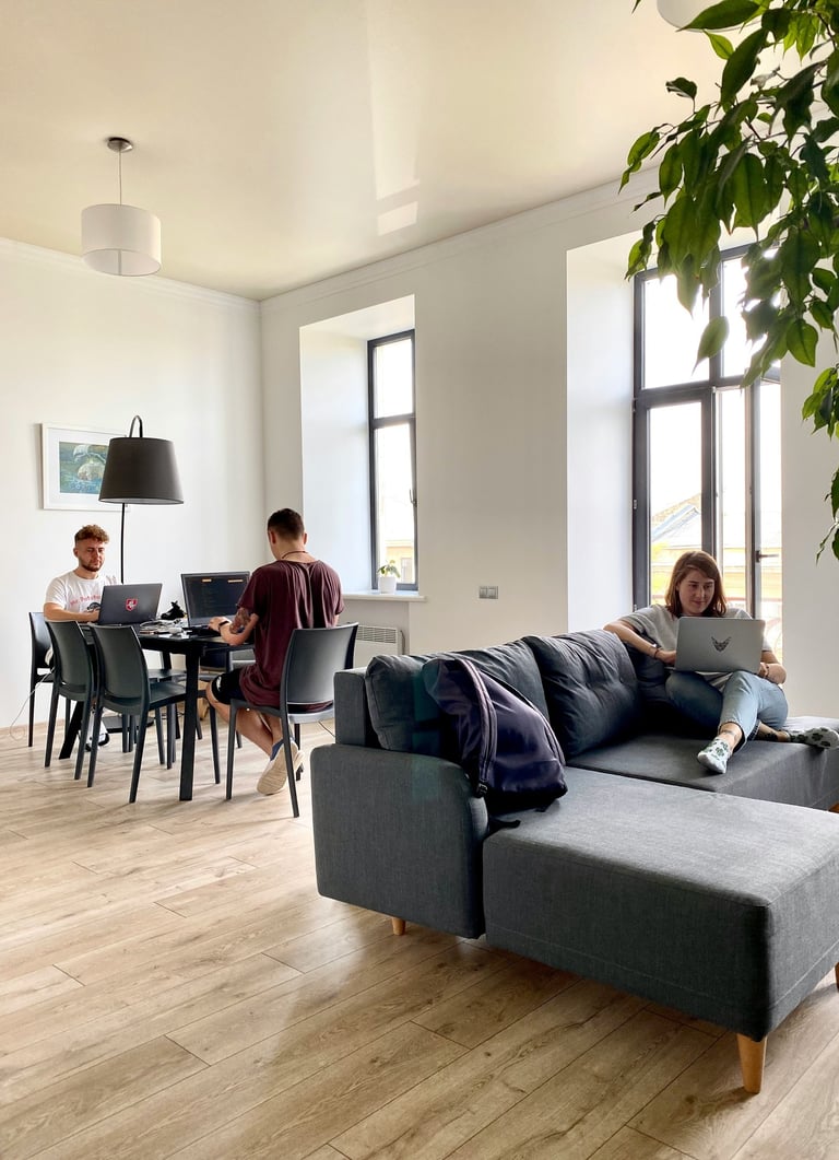 Young professionals working on laptops in a bright, modern open-plan office with a sofa and dining table.