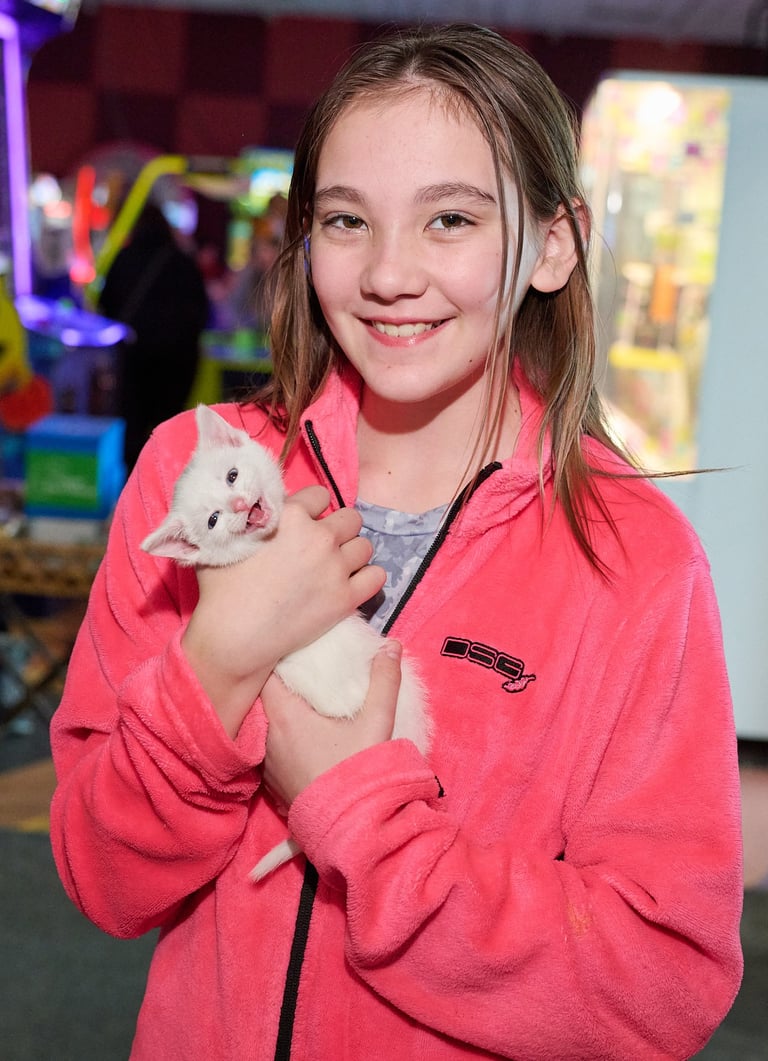 a girl in a pink jacket holding a white kitten